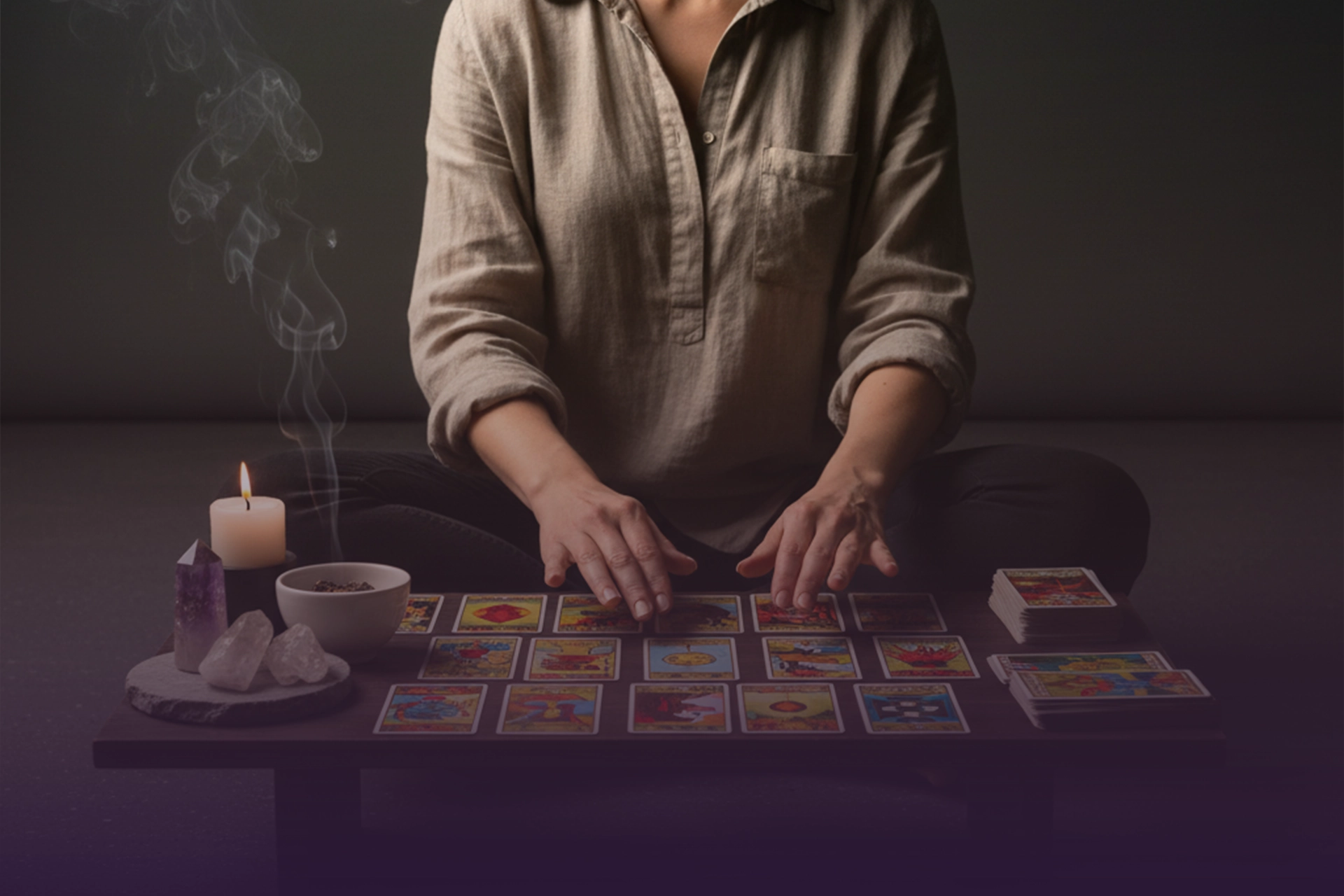 Manos sobre cartas de tarot en mesa con vela, cristales y humo de sahumerio.
