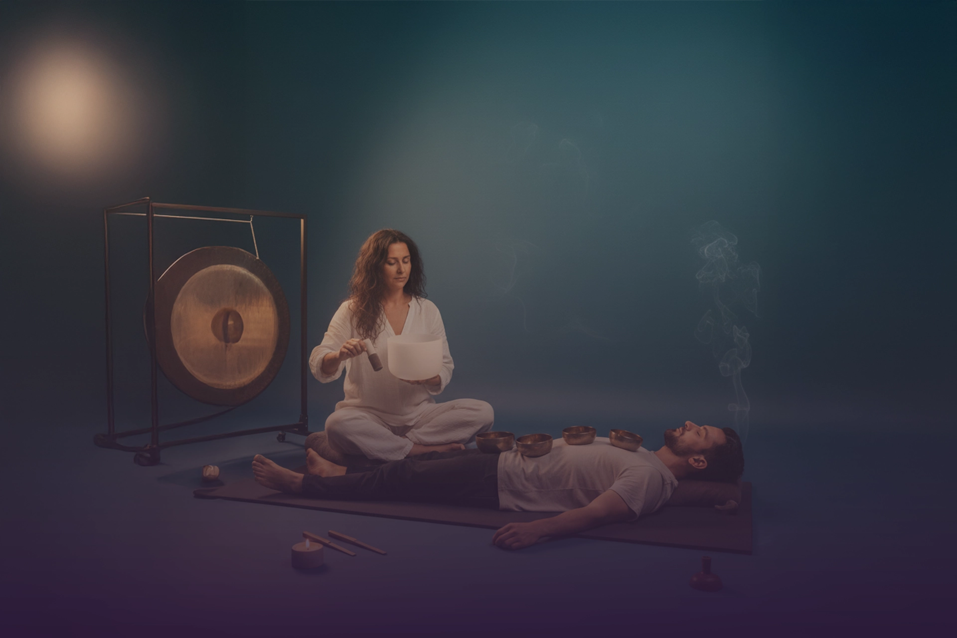 Terapeuta tocando cuenco de cristal junto a gong; persona recostada con cuencos tibetanos sobre el pecho e incienso humeante.